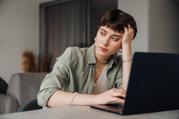 Tired young woman looking aside while working on laptop at home