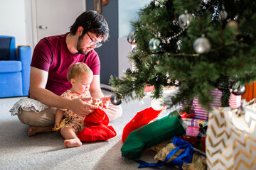 Christmas morning joy of first Christmas - baby with father unwrapping stocking gifts under tree