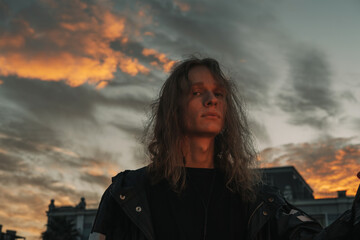 Close up Portrait of young man with long blond hair with sunset sky o background