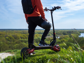 A young man on a powerful electric scooter to ride in the spring in the park. Drive to the hill overlooking the green forest . Spending time in nature