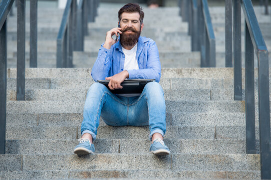 photo of guy talk on smartphone sit on stairs. guy talk on smartphone outdoor.