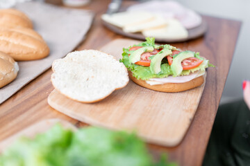A prepared healthy sandwich with lettuce, avocado and tomato is on the cutting board