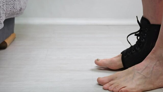 man with a leg injury in a fixing bandage walks and sits down relaxing his leg. sprained ligaments or leg injury during sports. slow motion. close up.