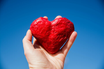 Mano sosteniendo un corazón rojo con fondo azul. San Valentin.