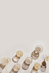 Flat lay with white sparkling wine bottle, set glasses wine with sunshine shadow and flare on light beige background. White wine aesthetic photo, copyspace. Summer holiday monochrome still life