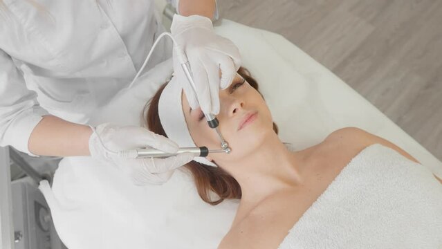 A beautiful woman receives a microcurrent facial skin treatment from cosmetologist in a spa salon. Doctor uses electrical pulses for cosmetic procedures to smooth out wrinkles, restore and rejuvenate