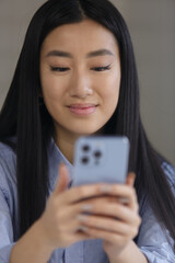 Portrait of beautiful Vietnamese BIPOC female typing sms message on smart phone. Cheerful Asian POC girl texting online with cellphone