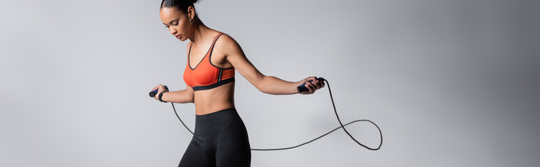 sportive african american woman exercising with skipping rope on grey background, banner. - obrazy, fototapety, plakaty