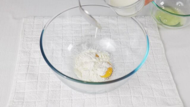 In a transparent bowl with eggs, I pour a tablespoon of milk to prepare the dough. High quality 4k footage