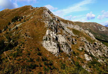 Panoramic view of the landscape with mountains and green hills in the foreground against a blue sky with clouds on Mount Cimetta, near Locarno in Switzerland