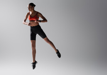 Fototapeta na wymiar full length of tattooed african american woman in sports bra and shorts jumping on grey background.
