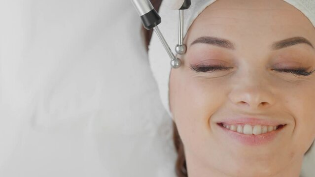 A beautiful woman receives a microcurrent facial skin treatment from cosmetologist in a spa salon. Doctor uses electrical pulses for cosmetic procedures to smooth out wrinkles, restore and rejuvenate