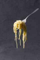 Fork with messy skein of spaghetti suspended on dark textured background.