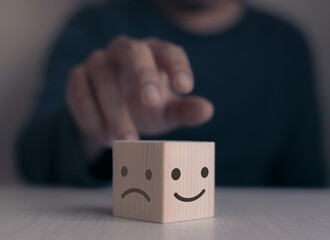 Customer hand picking smiley and sad face on wooden cube,customer service and satisfaction concept