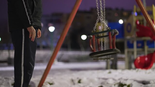 Mentally ill man on empty playground swing, concept of child abduction, cold winter night. State of emergency