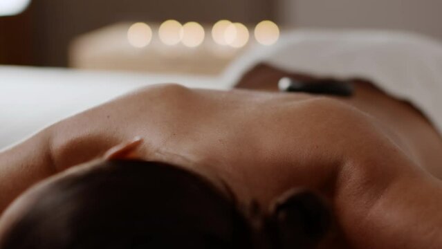 Spa relaxation concept. Close up shot of professional masseur putting hot stones on female back, free space