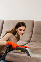 Cleaner girl is cleaning couch with extractor machine for dry clean upholstered furniture....
