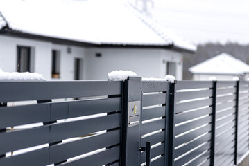 A modern videophone with a letterbox and a wireless card reader, mounted in panel fence in anthracite color, visible wicket, it rains in winter.