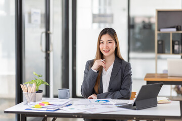 Young business Asian woman is sitting at table, working on laptop with graphs, charts, money and report financial concepts. Online marketing, education, analytics, e-commerce, business planning