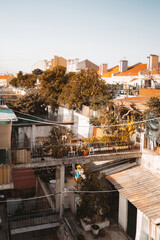 A vertical wide-angle drone view of a typical European courtyard with small bridges in between houses and patios, plenty of house plants and fruit trees, tiled clay roofs, clean blue sky, warm day