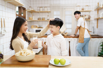 Asian cute little boy having a breakfast with his parent in a kitchen, boy holding a glass of milk and drink.