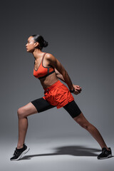 full length of brunette african american woman in sportswear and sneakers exercising on grey.