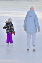 Mother and daughter skating on an outdoor ice rink on a winter day