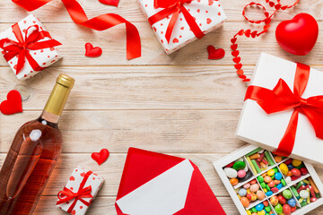 Fototapeta premium top view photo of st valentine day decor shopping, bag, wine, bottle, envelope, gift, box, candy and red heart on colored background with empty space. Frame background