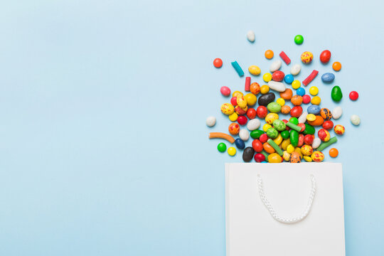 shopping paper gift bag in corner full of assorted traditional candies falling out on colored background with copy space. Happy Holidays sale concept