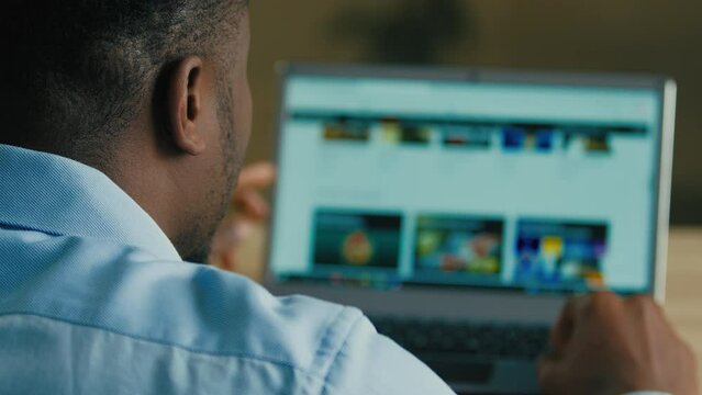 Backside Unknown Man African American Businessman Web Designer Employee Sit At Home Office Searching Films TV Series On Internet Website E-service Looking At Computer Laptop Screen Over Shoulder View