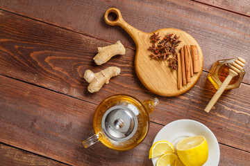Transparent teapot of lemongrass tea next to anise, ginger and cinnamon on a round wooden board and honey and lemon. view from above.