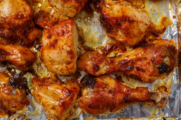 Baked chicken legs and breasts in sauce and herbs on foil close-up.