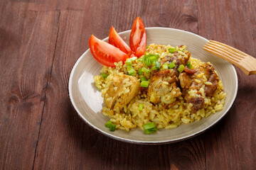 Thai chicken rice garnished with green onions on a wooden table next to a wooden fork.