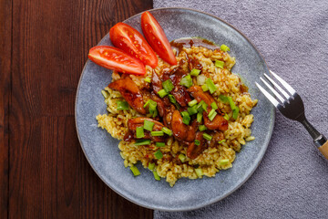 Rice chicken in teriyaki sauce garnished with green onions on a wooden table next to soy sauce on a napkin next to a fork.