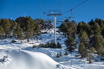 Ski resort lifts with skiers sitting on chairs to climb high in the mountains, Andorra.