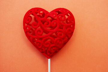 Red decorative gift heart on a stick on an orange background.