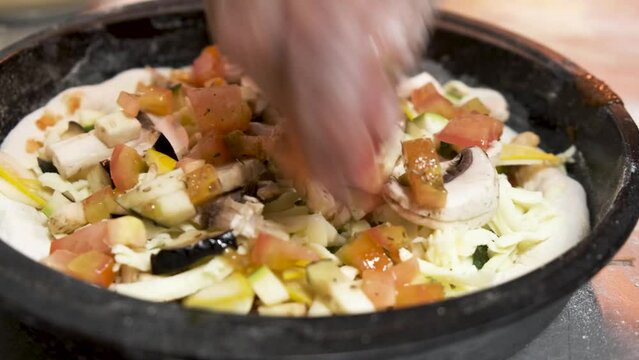 Manos del pizzero arrojando vegetales en la maza antes de ser horneada la pizza