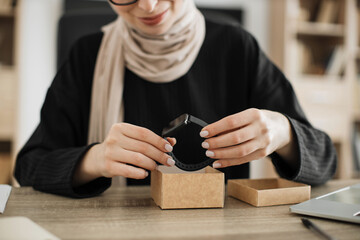 Cropped view of muslim woman doing live stream while unpacking box with new smart watch. Female...