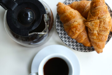 morning in a cozy apartment, on the table a kettle with fresh black coffee, a white cup and fresh croissants on a plate