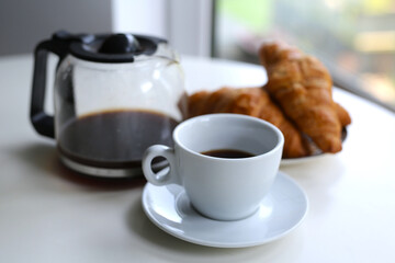 morning in a cozy apartment, on the table a kettle with fresh black coffee, a white cup and fresh croissants on a plate