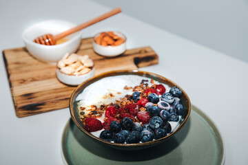 Yoghurts in green plate with blueberries, raspberries, chia seeds and granola with a wooden board on a white background