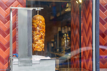 Shawarma kebab meat is fried on a spit behind glass on an electric heater