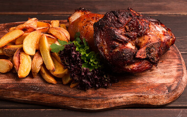Pork knuckle, in soy-honey sauce, with fried potatoes, on a wooden chopping board, homemade, no people, - obrazy, fototapety, plakaty