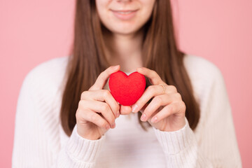 girl holding a heart in her hands close-up on a pink background, the concept of valentine's day