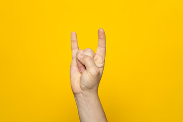 Naklejka premium Strong hand of man making the rock gesture on a yellow studio background.
