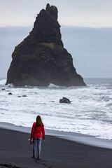 Beautiful girl in pink jacket walks and admires the big waves on famous stunning Reynisfjara Beach in southern Iceland