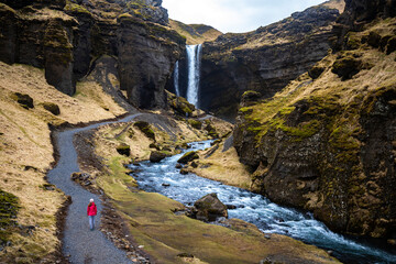 Girl in pink jacket walks to stunning famous Kvernufoss waterfall and river hidden in canyon in picturesque setting, Iceland