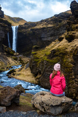 Naklejka premium Girl in pink jacket admires stunning famous Kvernufoss waterfall and river hidden in canyon in picturesque setting, Iceland
