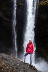 woman in pink jacket standing in front of powerfull icelandic waterfall - kvernufoss; hidden waterfall in inceland