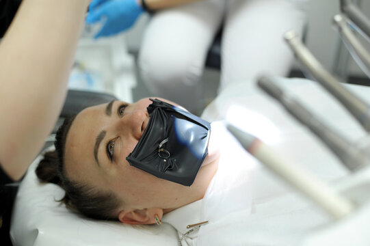 cofferdam clamp for cofferdam The process of dental prosthetics using a microscope, female doctor in gloves, patient dentist with patient, using dental curing light